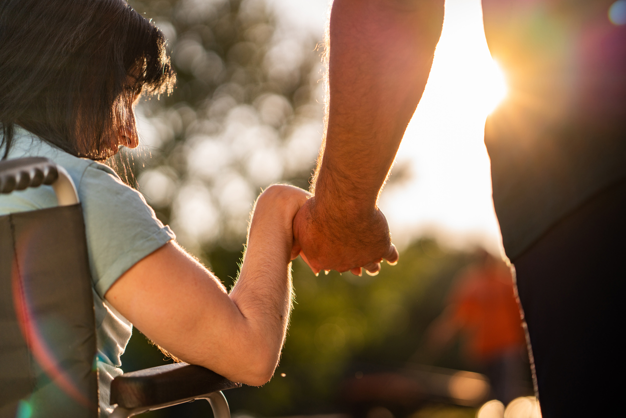 Close up image of women in a wheel chair holding friend's hand